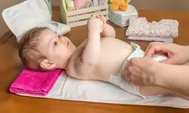 Mother changing diaper of adorable baby with a hygiene set for babies on the background